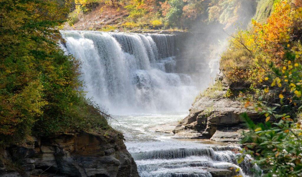 Powerful waterfall cascading over rocky cliffs surrounded by colorful autumn foliage in Letchworth State Park, New York.