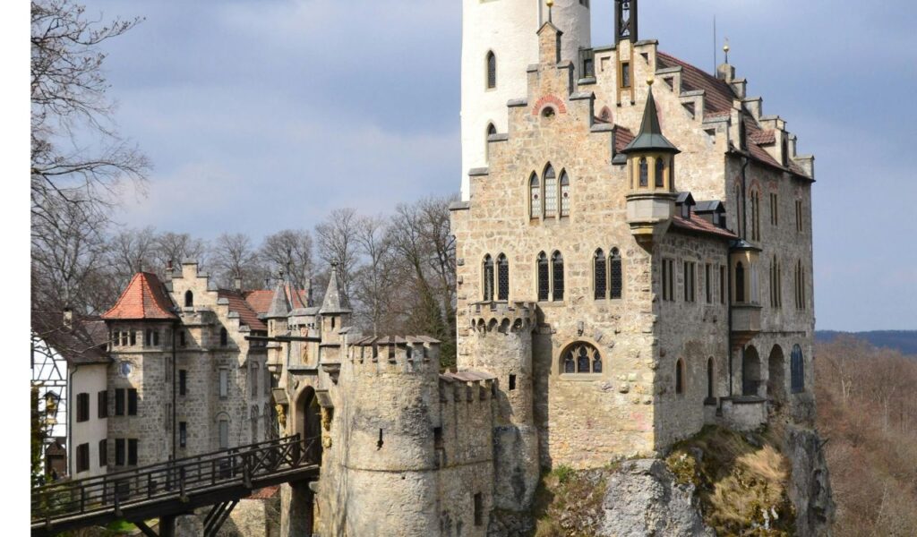 Lichtenstein Castle in Germany perched on a rocky cliff with stone walls, towers, and a wooden bridge leading to its entrance.