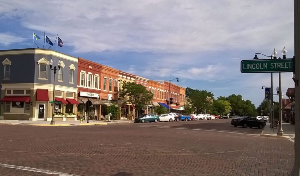 A quiet street view in Lindsborg, Kansas, shows brick-paved roads, historic storefronts with colorful awnings, and a Lincoln Street sign.