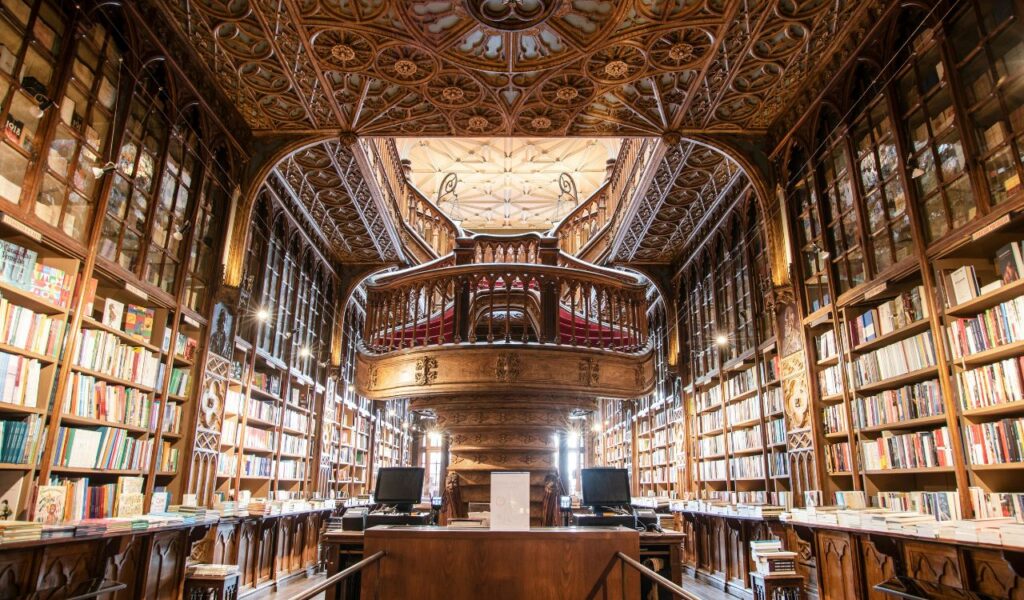 Ornate interior of Livraria Lello in Porto, Portugal, featuring a grand wooden staircase, carved ceilings, and bookshelves filled with colorful books.
