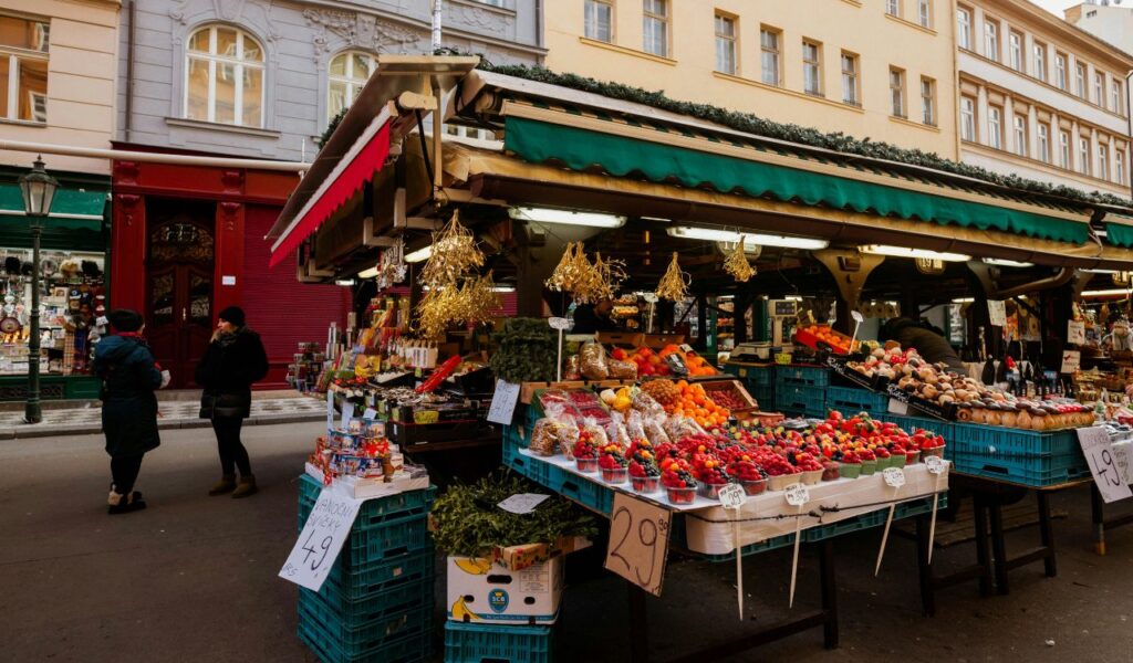 Outdoor farmers market in Market Square, Knoxville, Tennessee, with stalls displaying fresh fruits, vegetables, and local goods under green awnings, and shoppers browsing on a sunny day.