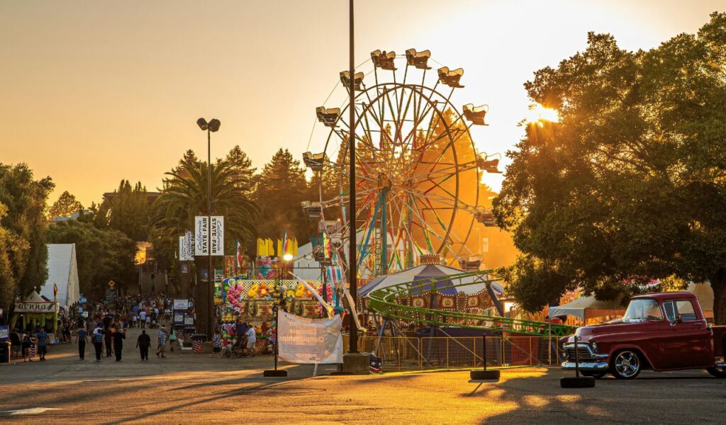 Minnesota State Fair at sunset with a Ferris wheel, carnival rides, game booths, and people enjoying the lively atmosphere.