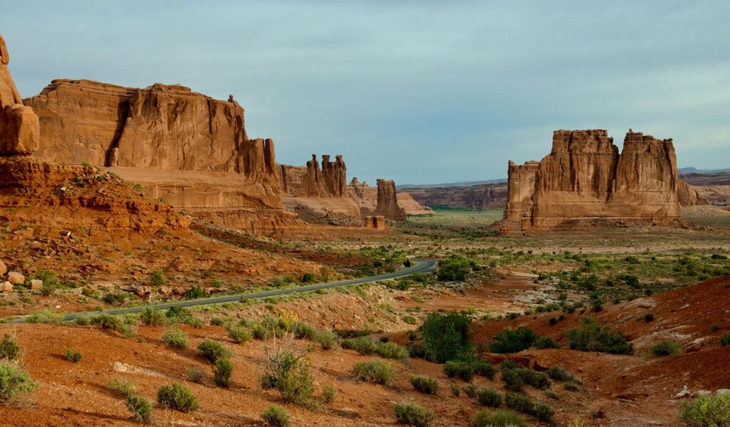Scenic desert landscape near Moab, Utah, featuring red rock formations, a winding road, and scattered desert vegetation under a cloudy sky