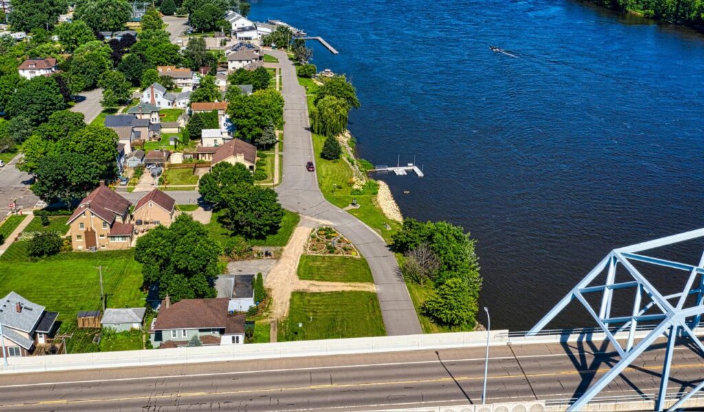 Aerial view of Natchez, Mississippi, showing riverside homes, green trees, and a bridge crossing the Mississippi River on a sunny day