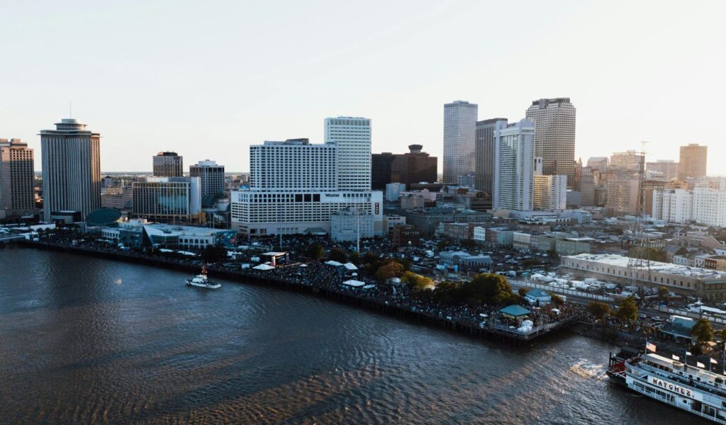 Aerial view of downtown New Orleans, Louisiana, showing high-rise buildings along the Mississippi River waterfront with a boat cruising nearby