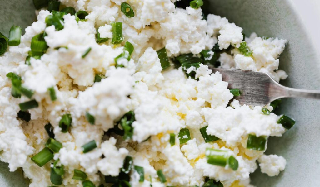 Close-up of cottage cheese mixed with chopped green onions in a bowl with a fork.