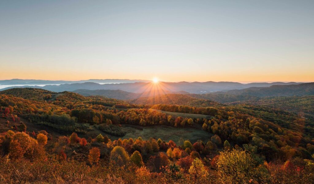 Sunrise over rolling forested hills in Pisgah, North Carolina, with autumn foliage in shades of red, orange, and yellow stretching into the distance