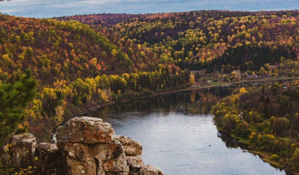 Rocky cliff overlooks a winding river bordered by dense forest in peak autumn colors in Michigan’s Upper Peninsula.
