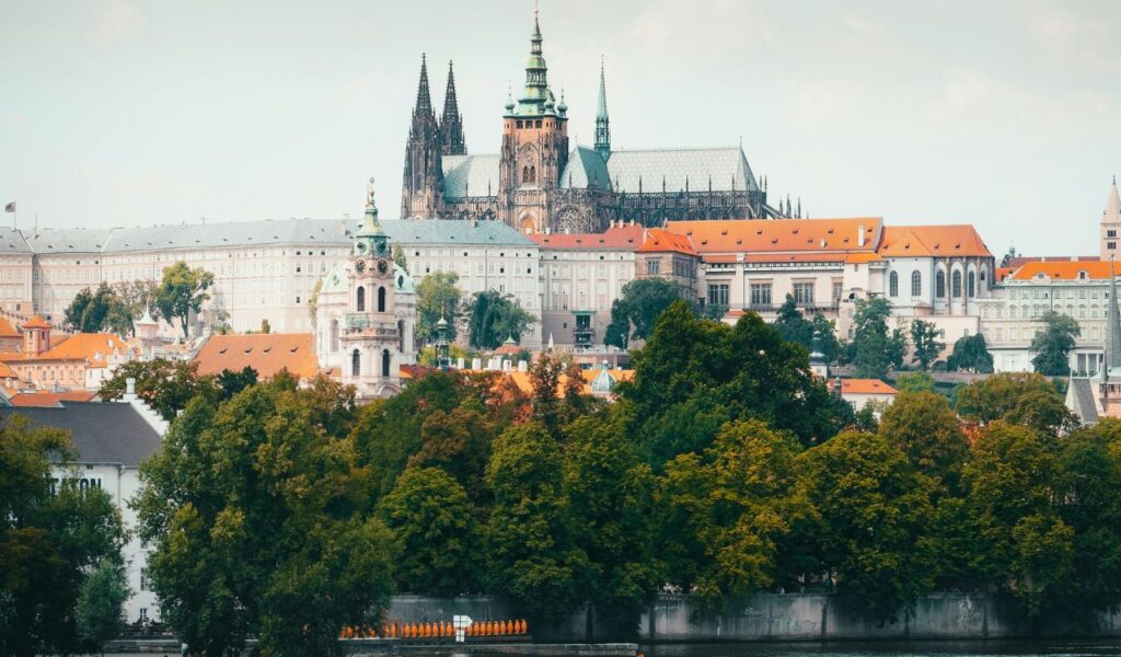 Prague Castle in the Czech Republic, featuring gothic spires and historic buildings with red rooftops, surrounded by lush green trees.