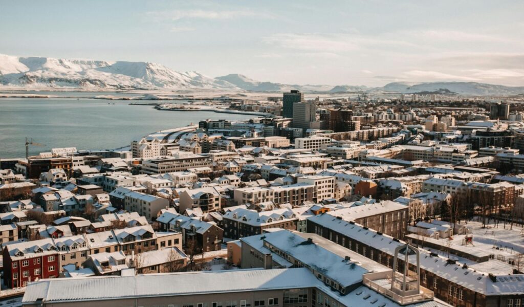 Snow-covered Reykjavik with colorful houses and modern buildings set against a backdrop of mountains and the North Atlantic Ocean.