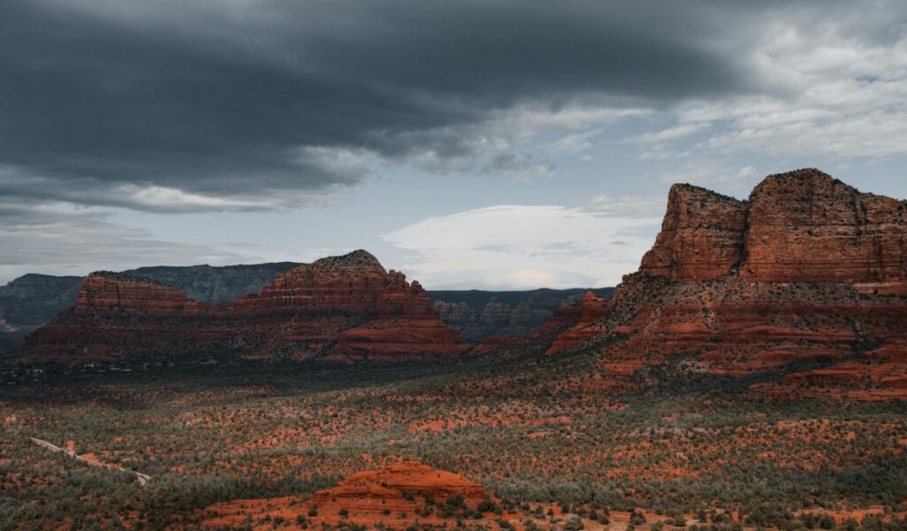 Dramatic view of Sedona, Arizona’s red rock formations under a moody sky, with rugged cliffs and desert vegetation stretching across the landscape.