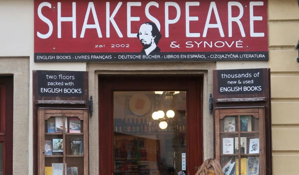 Entrance of Shakespeare and Company bookstore in Paris, featuring a red sign with white lettering and display windows filled with books.