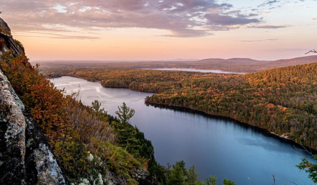 Autumn view over Shawnee State Forest with colorful trees, rocky cliffs, and a lake stretching into the distance.