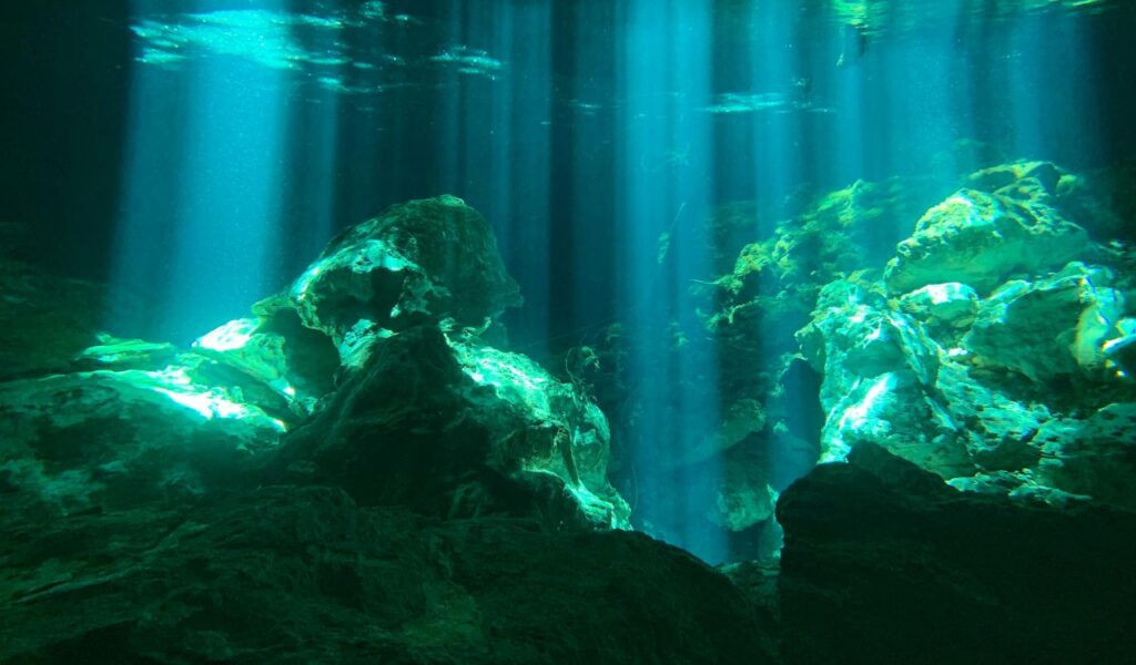 Sunlight streams through clear blue water, illuminating rocky formations inside Sicily’s underwater caves, creating a mystical and serene view.