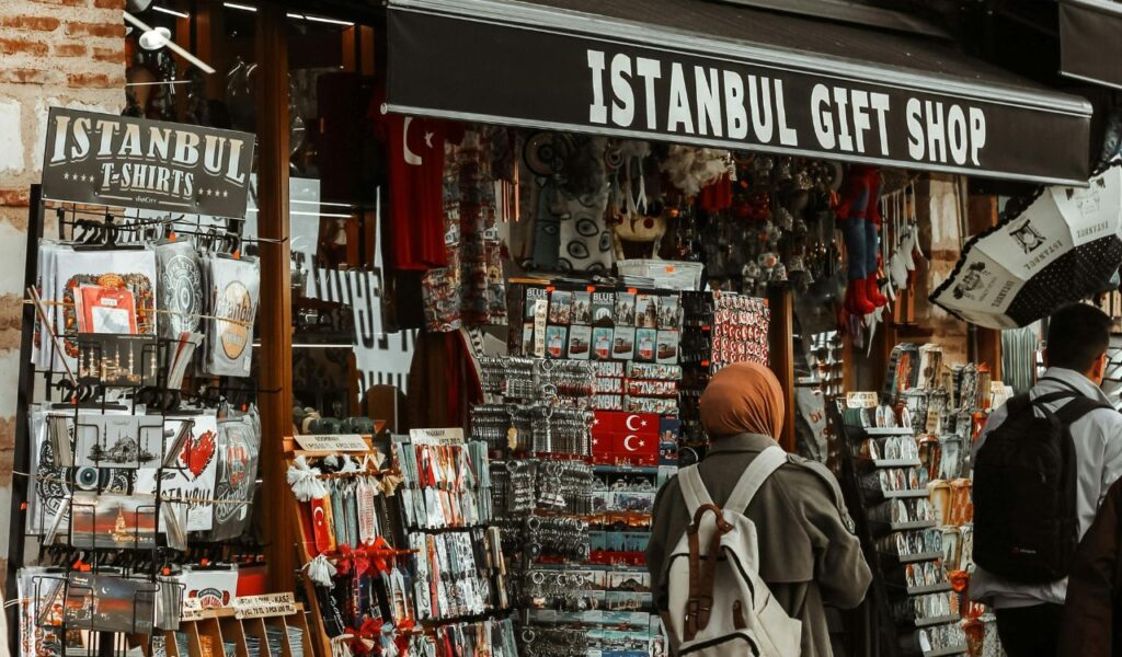 Tourists browsing an Istanbul gift shop filled with souvenirs, T-shirts, and trinkets marketed as local cultural items