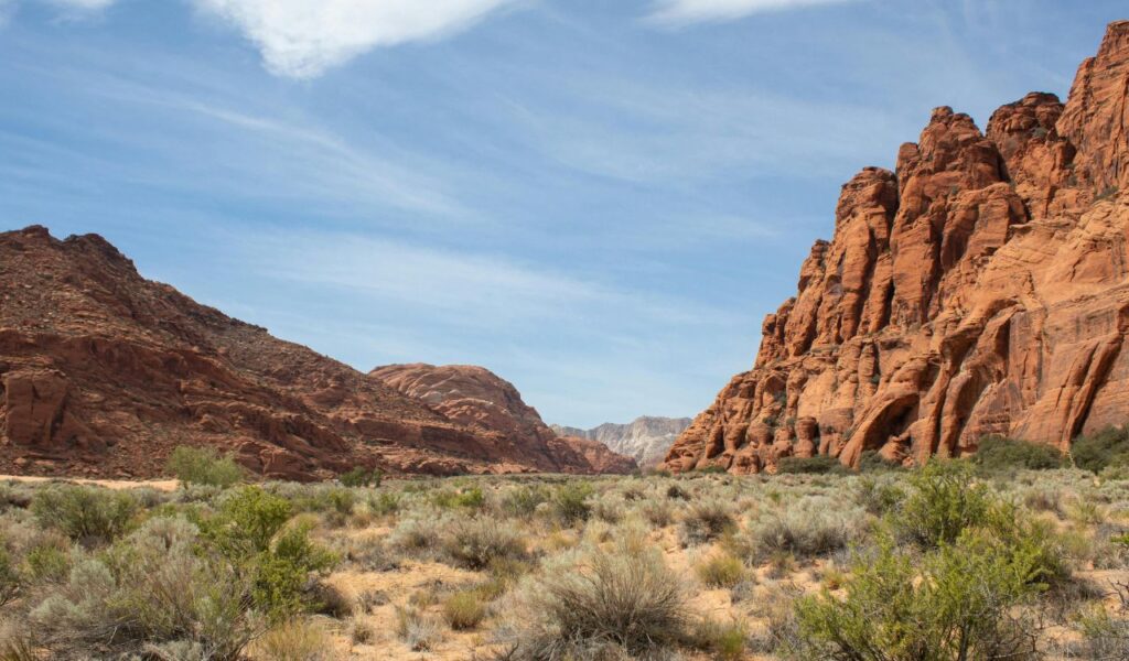 Desert landscape near St. George, Utah, with rugged red rock cliffs, dry vegetation, and a blue sky with light clouds