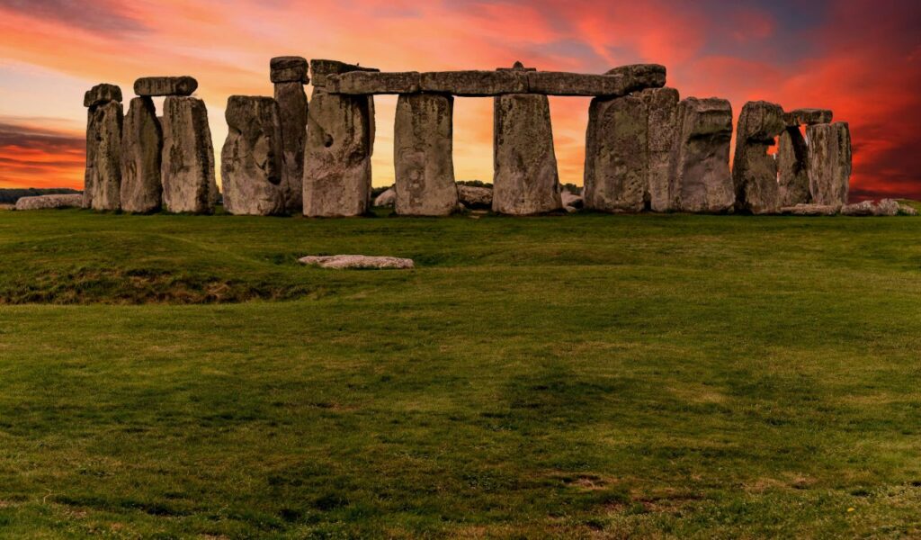 Stonehenge in England under a dramatic sunset sky, with ancient stone structures standing on a grassy plain.