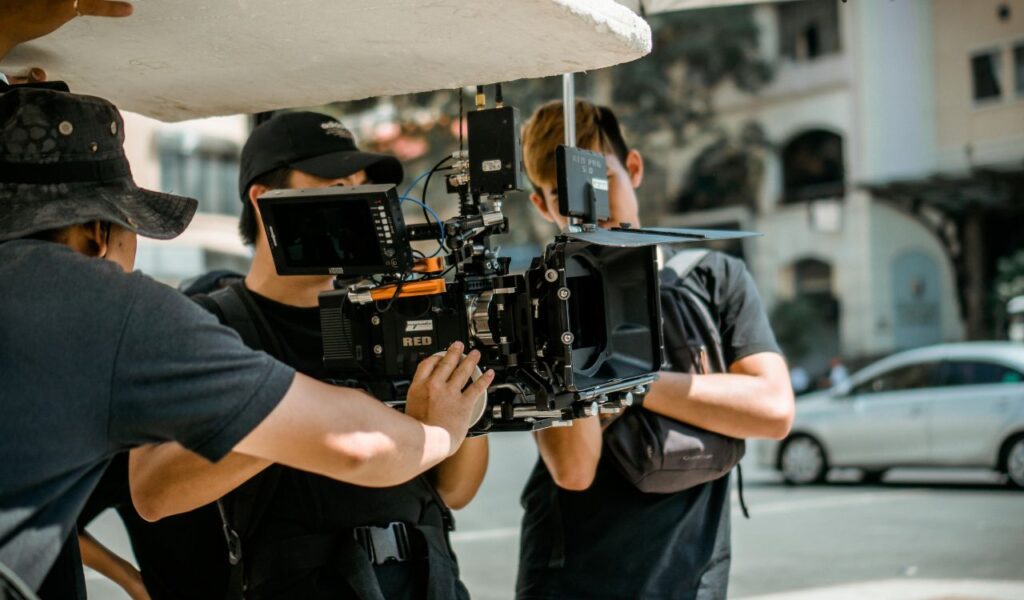  Film crew operating a RED cinema camera outdoors, adjusting settings and preparing for a shoot.