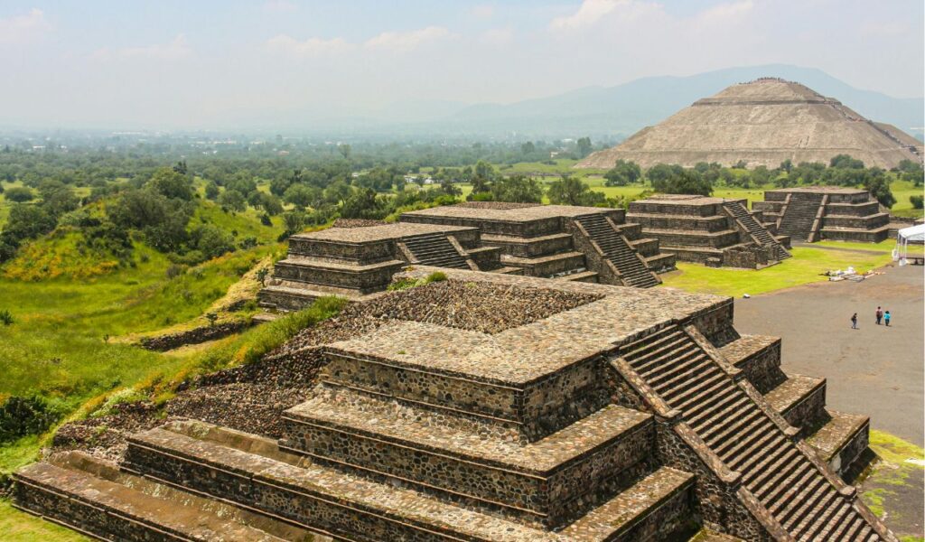 Ancient stepped pyramids of Teotihuacan in Mexico, surrounded by lush green landscape, with the Pyramid of the Sun visible in the background.