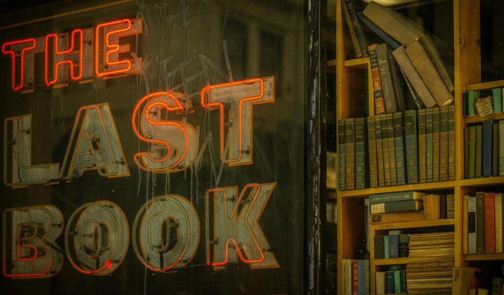 Neon sign reading "The Last Book" beside wooden shelves filled with vintage books at The Last Bookstore in Los Angeles.