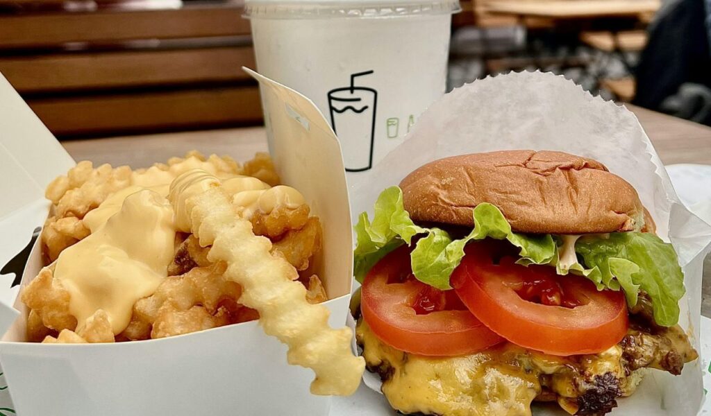 Cheeseburger with lettuce and tomato served with cheese fries and a drink as part of a tourist meal deal.