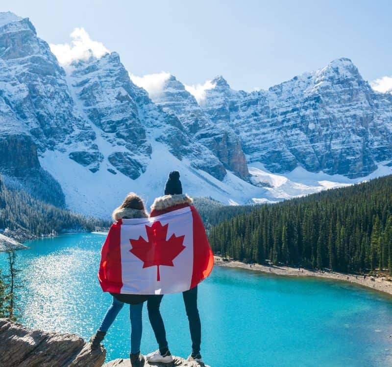 Tourists draped in Canadian flag looking beautiful scenery of Moraine lake. Banff National Park. Canadian Rockies. Alberta, Canada.