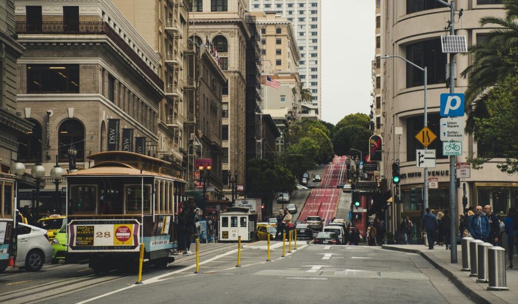 Street view of San Francisco’s iconic cable cars traveling uphill near Union Square, surrounded by historic buildings, shops, and pedestrians.