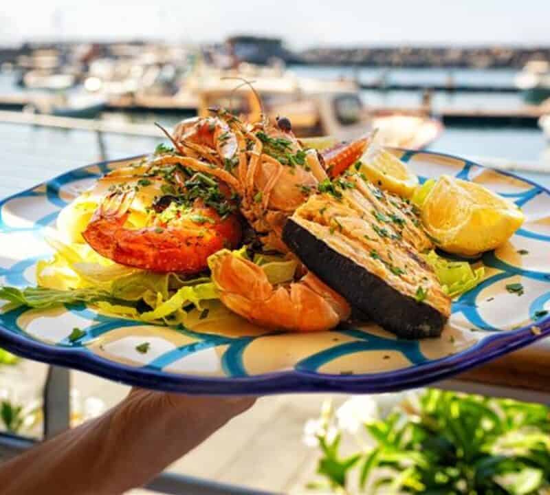 Serving Seafood and fish lunch in sea coast restaurant, Sicily, Italy. Italian food. Outdoor. Port with yacht on background