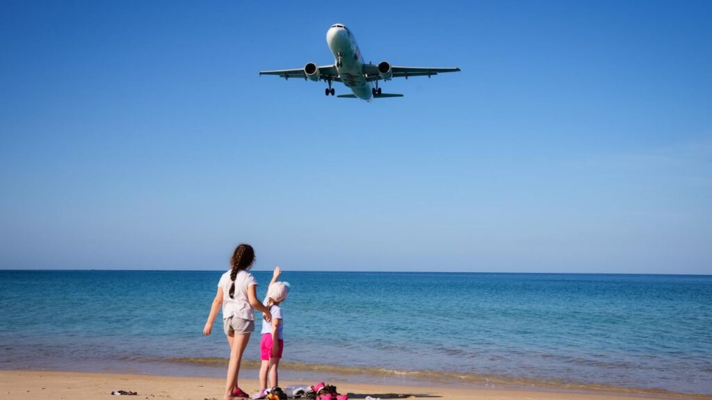Phuket, Thailand. January 12,2019. Two girl kids at the beach are interesting to see the airplane landing near Phuket International Airport.