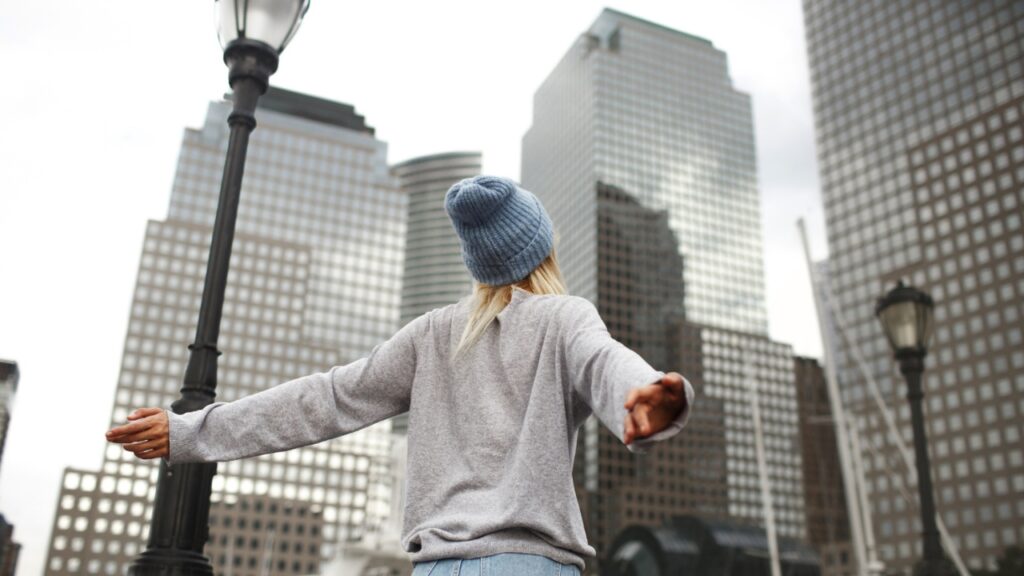Girl in blue hat and grey sweater stands on the street with skyscrapers