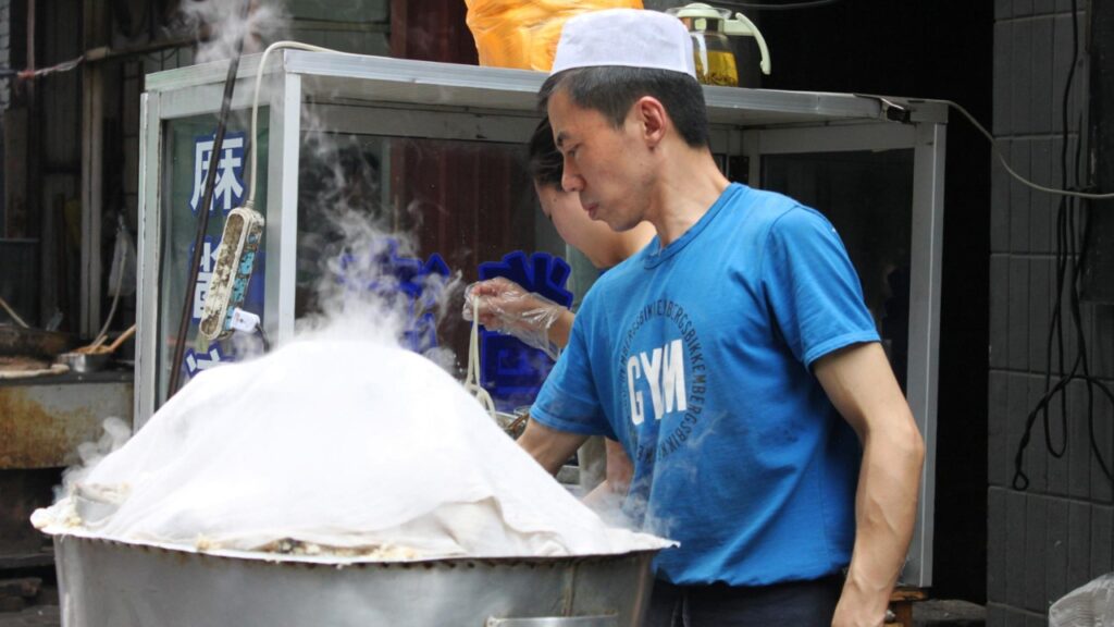 Xi’an, China – June 01, 2011: A street food vendor steaming buns in a large pot covered with a white cloth in a street food setting