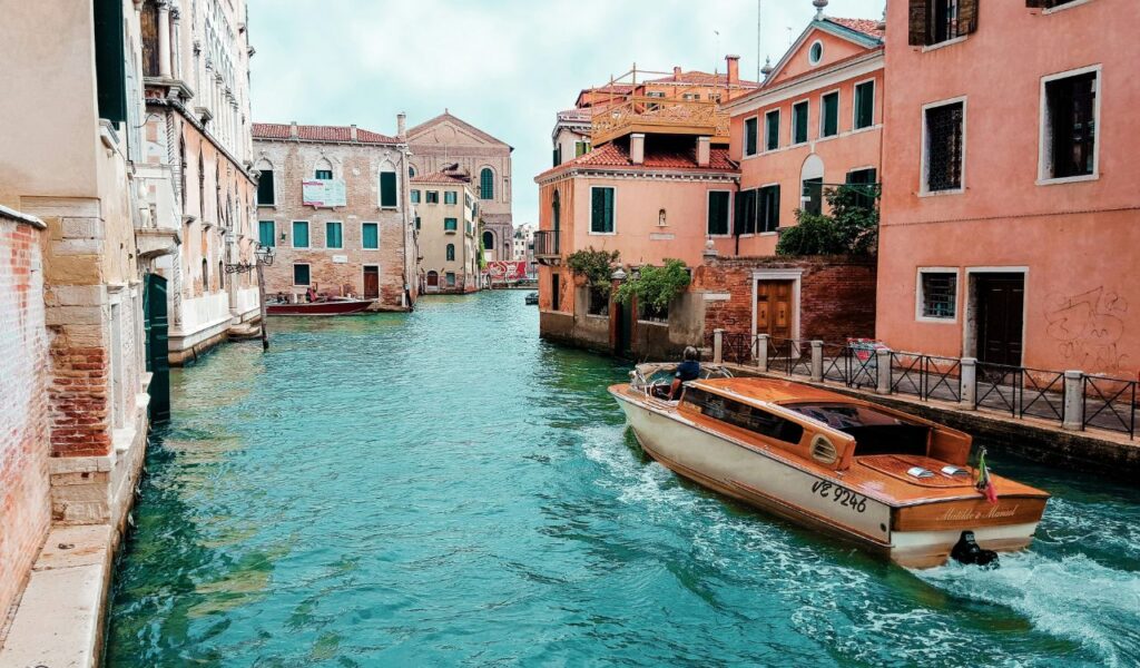 Wooden boat cruising through a turquoise canal in Venice, surrounded by colorful historic buildings.