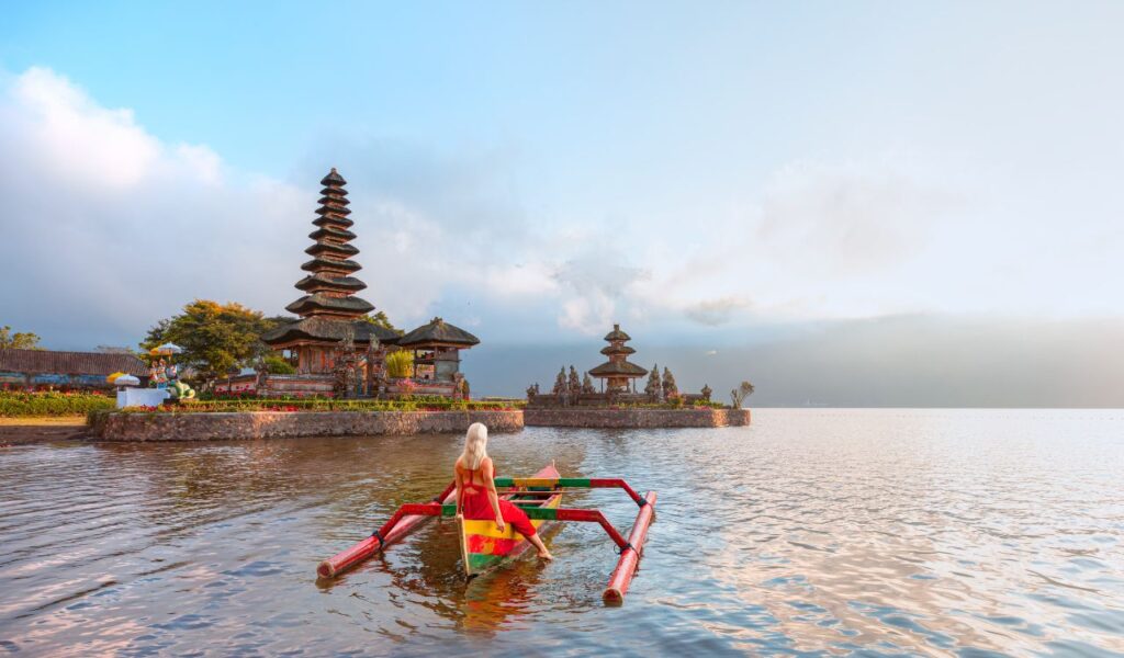 Young blonde girl in traditional red dress in the boat near Pura Ulun Danu Bratan temple - Hindu temple on Bratan lake - Bali island, Indonesia