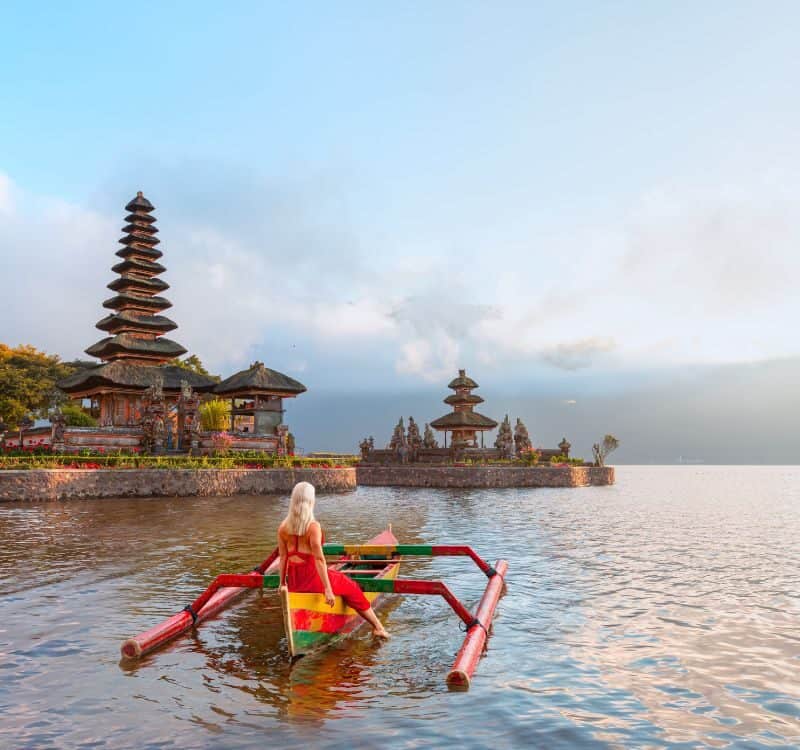 Young blonde girl in traditional red dress in the boat near Pura Ulun Danu Bratan temple - Hindu temple on Bratan lake - Bali island, Indonesia