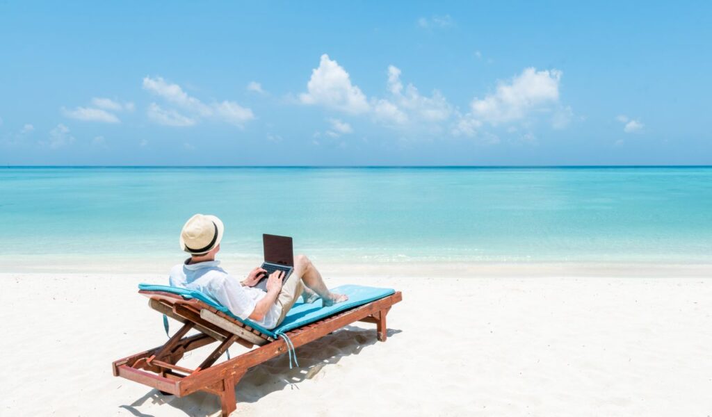 Young man working as digital nomad on the beach with a laptop