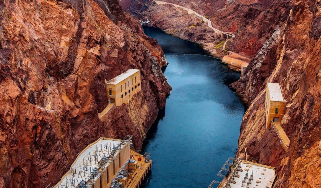 View of Hoover Dam's inner canyon with power station buildings built into the rocky cliffs beside the Colorado River.