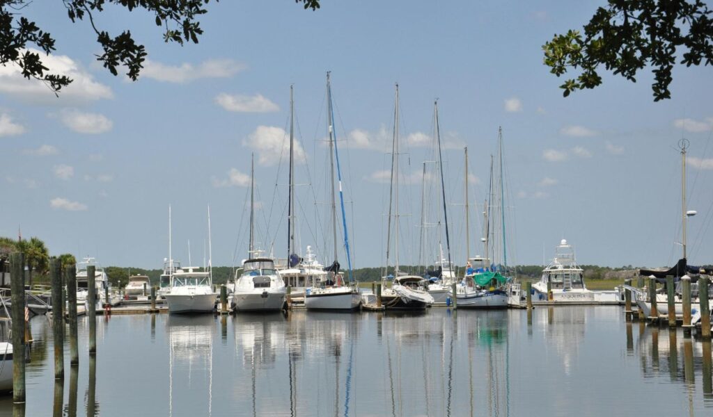 Sailboats and yachts docked at a calm marina on Amelia Island, Florida, with clear blue skies and reflections on the water.
