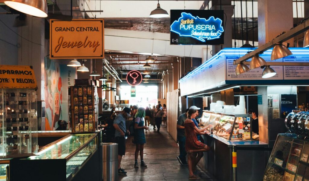 People order food at Sorrita’s Pupuseria inside Asheville’s Grand Central-style market, surrounded by jewelry stalls and neon signs.