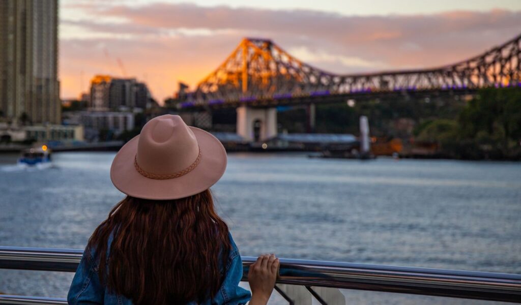 back view of a long hair woman in a hat watching the sunset over brisbane city