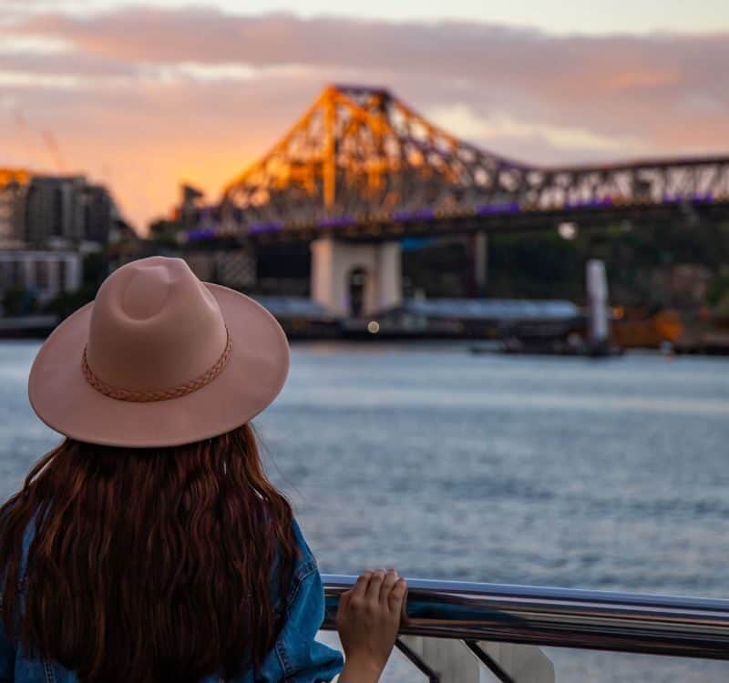 back view of a long hair woman in a hat watching the sunset over brisbane city