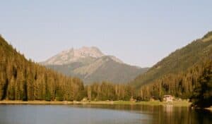 Tranquil lake in Bellaire, Michigan, surrounded by dense evergreen forests with mountain peaks in the background under a clear sky.