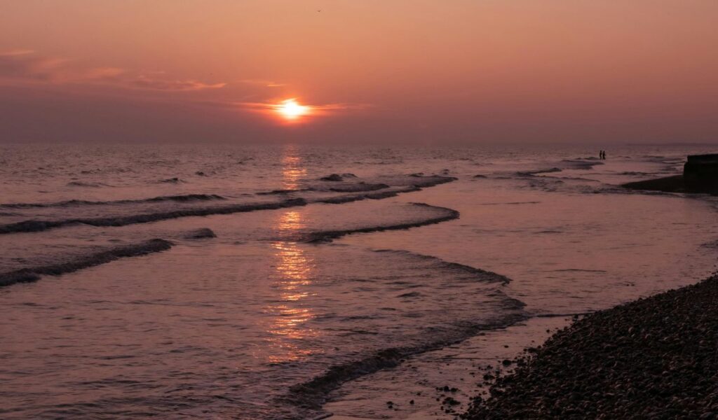  Tranquil sunset over the sea at Brighton, with gentle waves rolling onto the pebble beach and a warm orange sky.