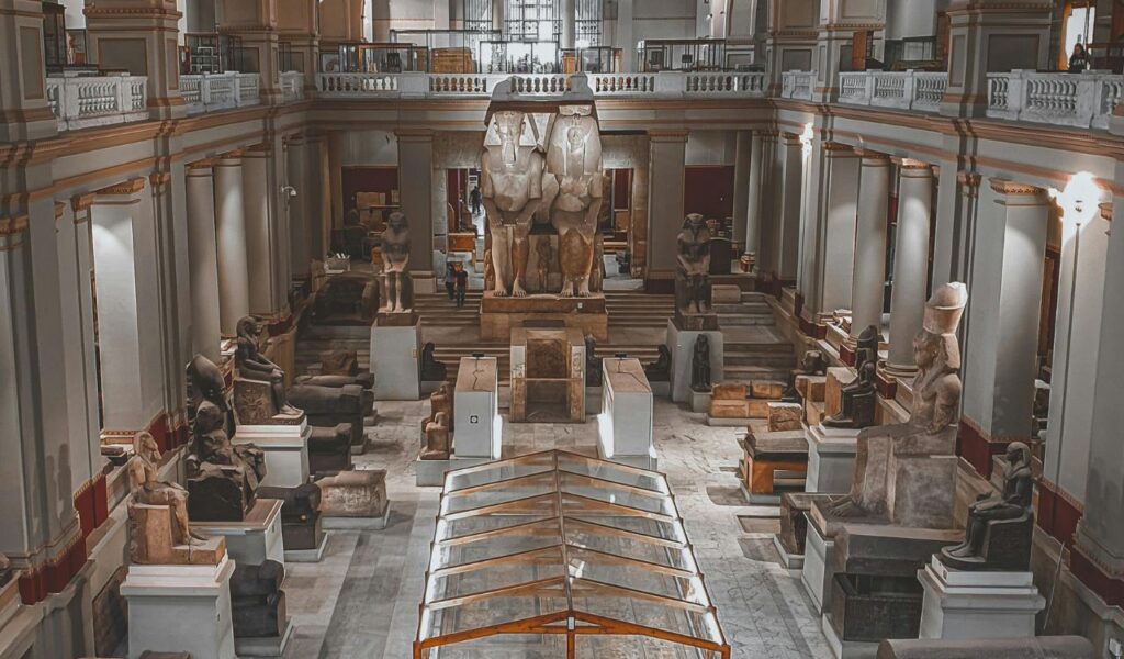 Interior of the Egyptian Museum in Cairo showcasing ancient statues, stone artifacts, and monumental sculptures arranged in a grand hall with tall columns.