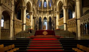 Ornate interior of Canterbury Cathedral with tall stone arches, stained glass windows, and a red-carpeted altar at the center.