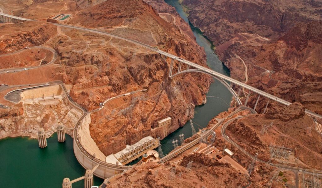 Aerial view of Hoover Dam and surrounding rocky terrain with a bridge spanning the Colorado River.