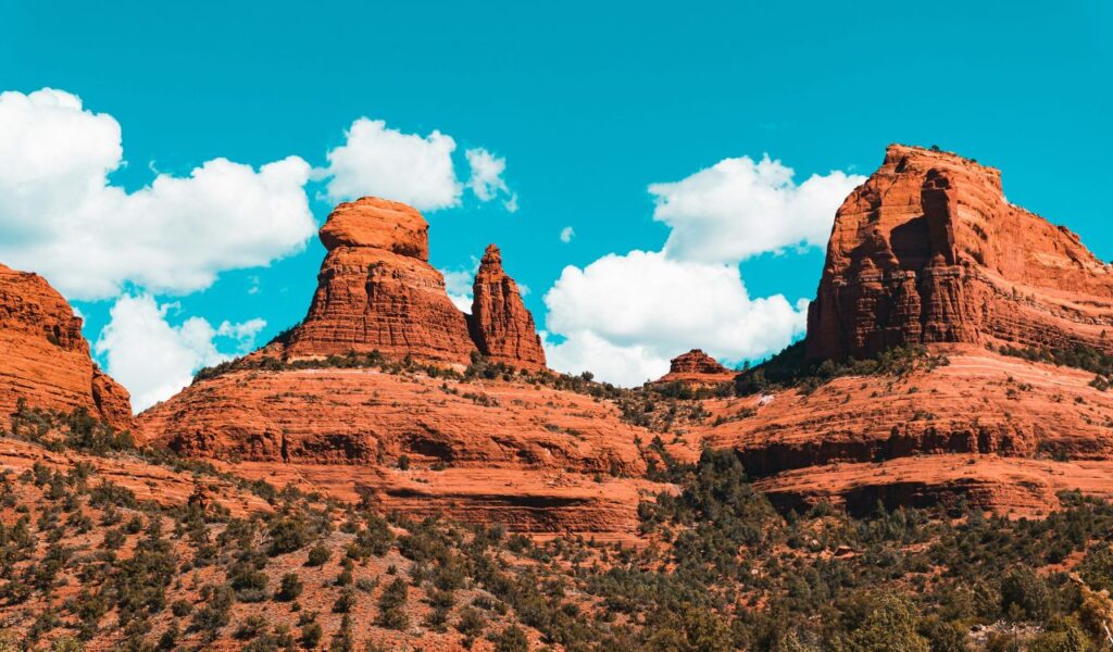 Stunning view of Sedona’s red rock formations under a bright blue sky with scattered white clouds, surrounded by desert vegetation
