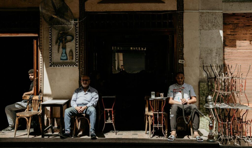 Locals relax outside a traditional Egyptian café, drinking tea and smoking shisha in the afternoon sun.