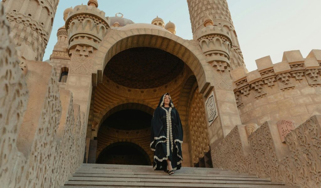Woman in modest black robe with head covering walks down steps of a historic mosque in Egypt, showcasing respectful travel attire.