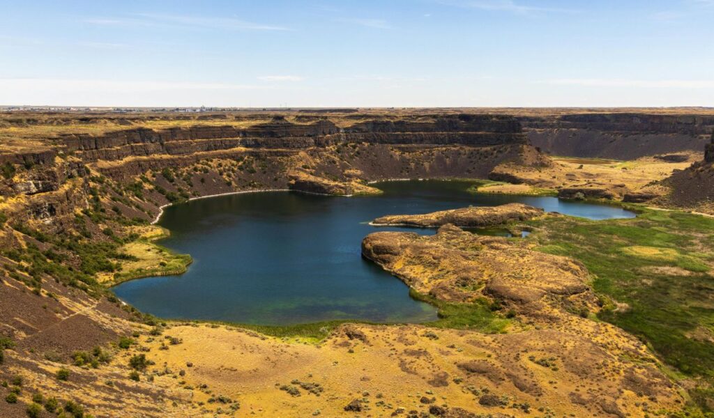 Aerial view of Dry Falls in Washington, showcasing a vast cliff-lined basin with deep blue lakes surrounded by golden, rocky terrain.