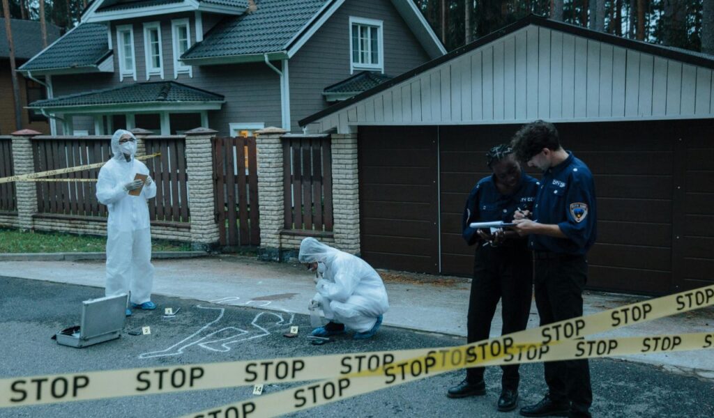 Police officers and forensic investigators work at a residential crime scene marked with yellow tape, evidence markers, and a chalk outline.